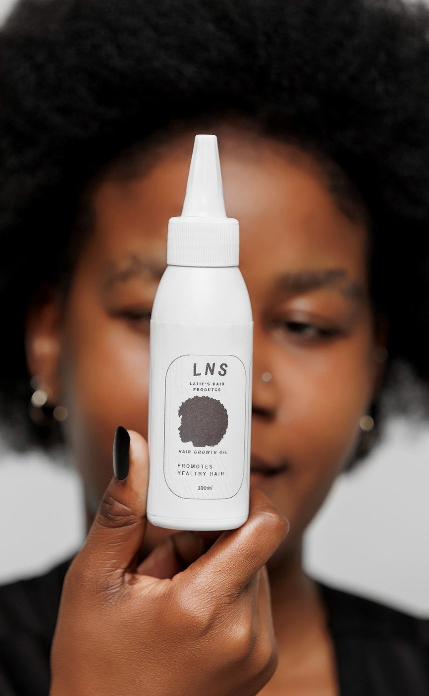 LNS Hair Growth Oil bottle held in front of natural hair